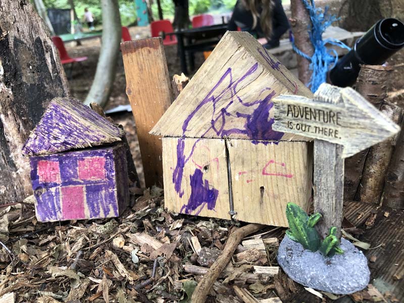 Wooden block houses with hand painted scribble in purple and pink on the wood chipped ground Surrey Hills Forest School